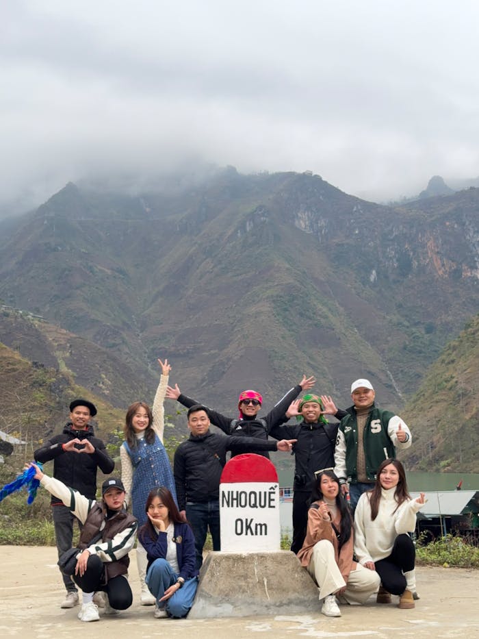 A joyful group poses at the Nho Quê 0km marker with stunning mountain views in Vietnam.