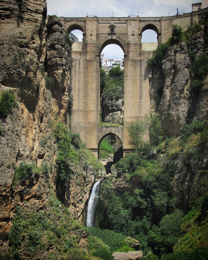 Stunning historical bridge over a lush gorge with waterfall, showcasing classic European architecture in a picturesque landscape.