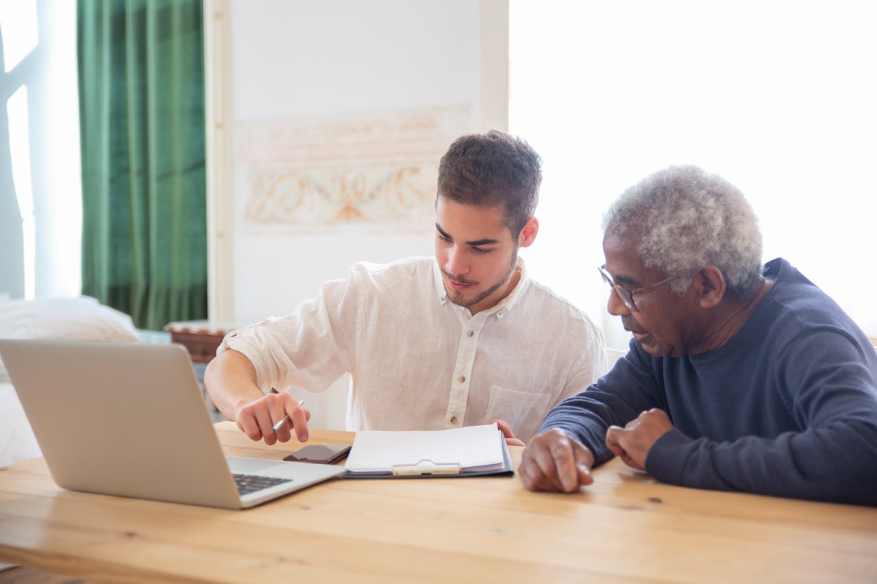 Young man teaches elderly gentleman to use technology at home.