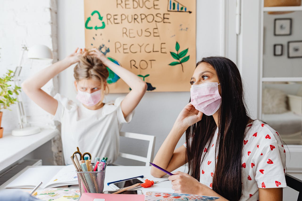 Two teenagers wearing masks work on an eco project indoors, focusing on sustainability.