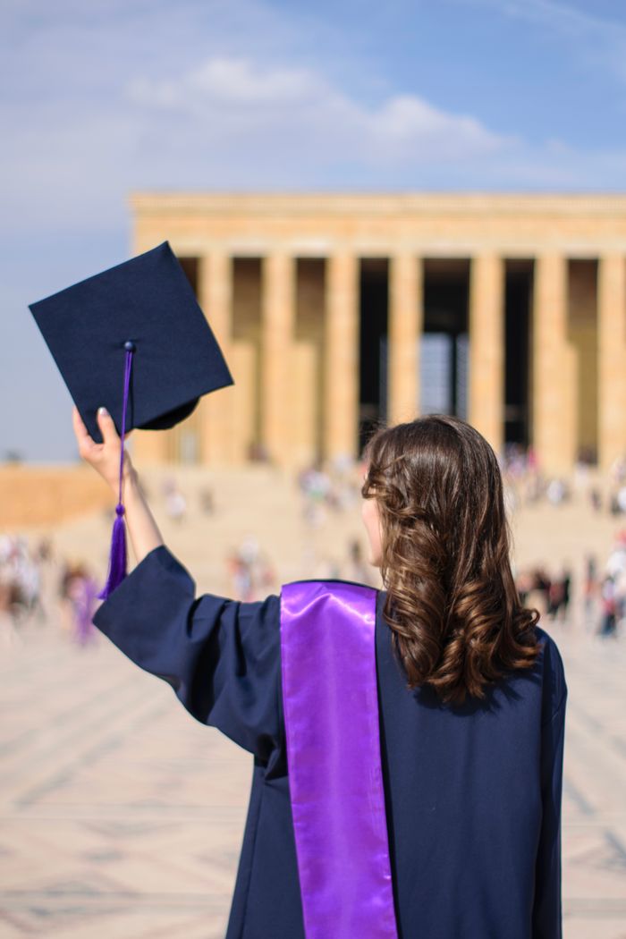A graduate stands proudly outside Anıtkabir, wearing a gown and mortarboard.
